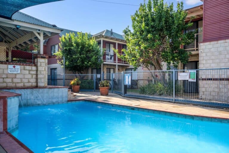 The outdoor pool at Amalfi Resort, a self-contained beach resort in Busselton, with resort villas and mature garden trees in the background.